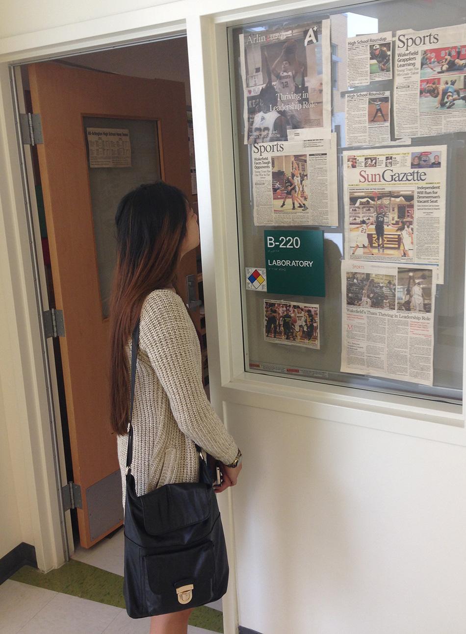 Senior Cathleen Madlansacay reads the sports clippings that Mr. Harris has posted outside his room.