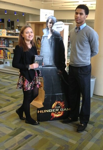 The two article authors pose with the famous Katniss Cut Out in the library before surveying the students for 2013 movie picks. 