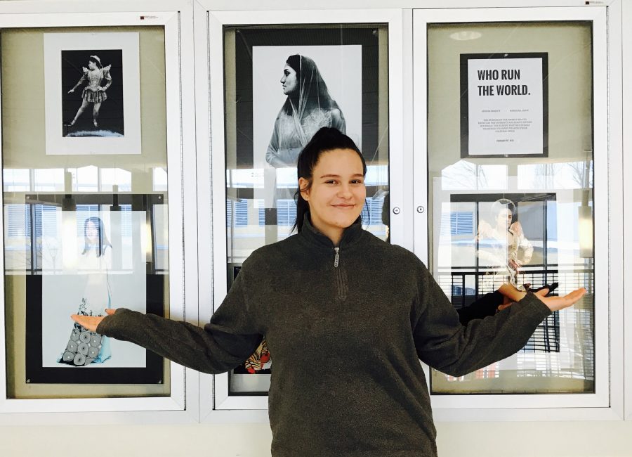 Karolina Lajch posing in front of the display of her photographs in the world languages hallway.
